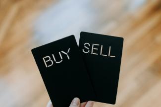 a hand holding two black cards with the words buy and sell written on them by Kelly Sikkema courtesy of Unsplash.