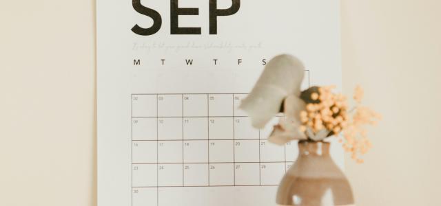 a desk with a calendar and a vase of flowers by Maddi Bazzocco courtesy of Unsplash.