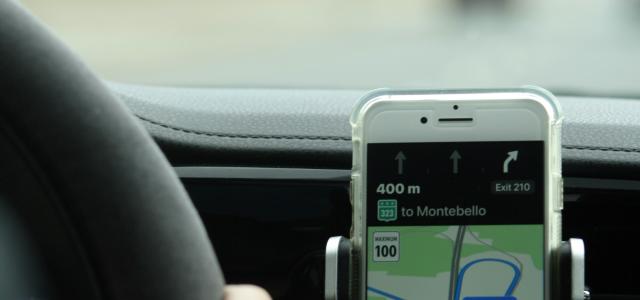 a person holding a cell phone while driving a car by capnsnap courtesy of Unsplash.