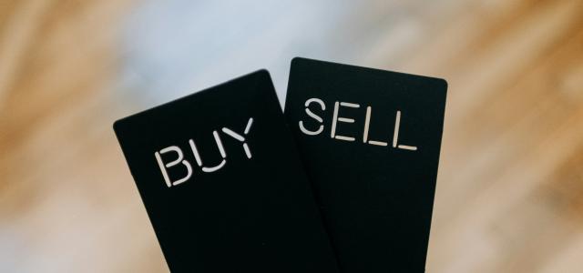 a hand holding two black cards with the words buy and sell written on them by Kelly Sikkema courtesy of Unsplash.
